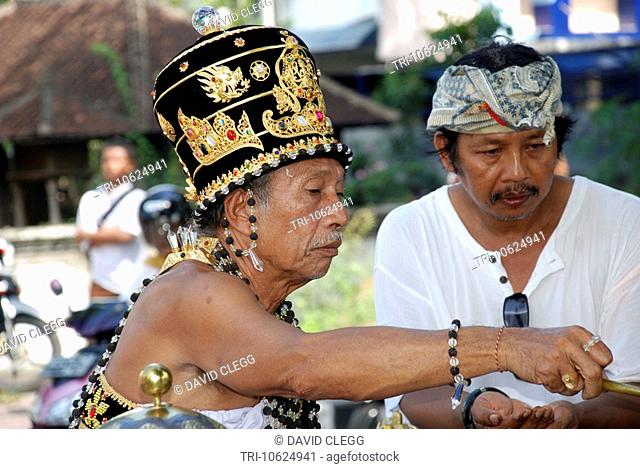 Head and shoulders of pedanda or Hindu priest wearing an ornate black and gold jewelled headdress blessing family member in Balinese cremation ceremony
