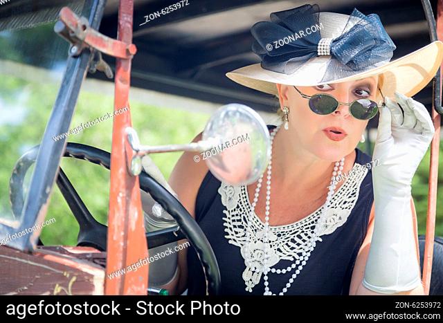 Attractive Young Woman in Twenties Outfit Checking Makeup in Antique Automobile