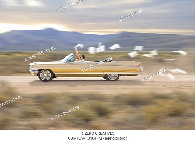 Convertible car, young couple, flying paper