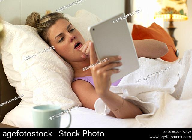 Coughing young woman in her bed with using tablet to check in with doctor