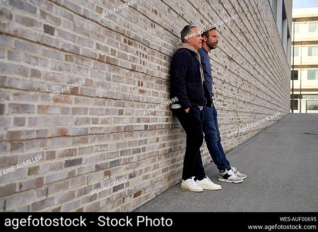 Mature businessmen talking with each other while leaning on wall