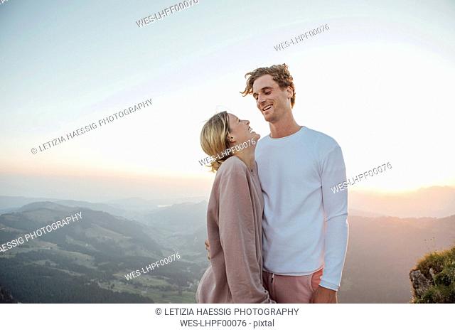 Switzerland, Grosser Mythen, happy young couple standing in mountainscape at sunrise