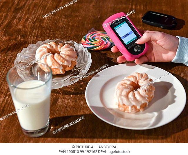 28 February 2019, Berlin: ILLUSTRATION - A girl is holding a remote control (PDM) for the mylife Omnipod tubeless insulin pump next to plates with cake