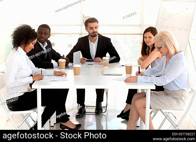 Excited diverse employees watch new workers sign contract at business meeting in office, female interns put signature on agreement closing deal at briefing