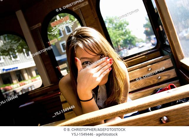 Young Asian female sitting inside a trolley, hiding her face behind hand