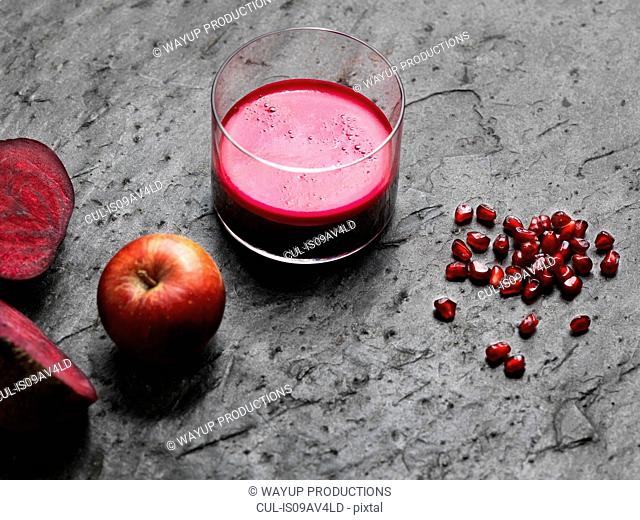 High angle view of purple raw juice, halved beetroot, apple and pomegranate seeds