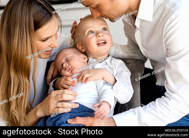 Mother and father taking care of baby boys sitting on chair at home