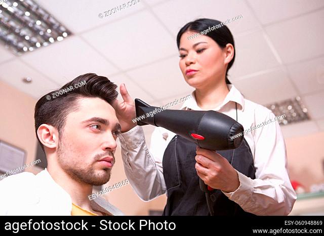 CLoseup side view picture of handsome man in hairdressing saloon. Hairdresser drying man#39;s hair with hair dryer