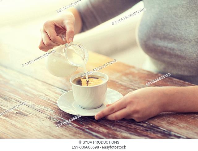 food and home concept - close up of female pouring milk into coffee