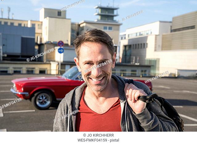 Portrait of smiling mature man in front of his sports car on parking level