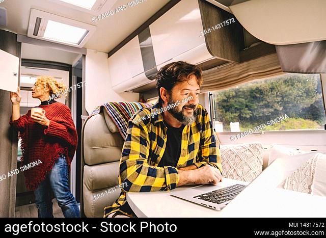 Couple traveling by camper van, man sitting in front of laptop, woman in background