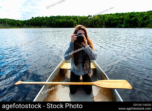 Young female photographer kneeling over knee is canoe clicking pictures with DSLR camera while on lake in Northern Quebec in Canada