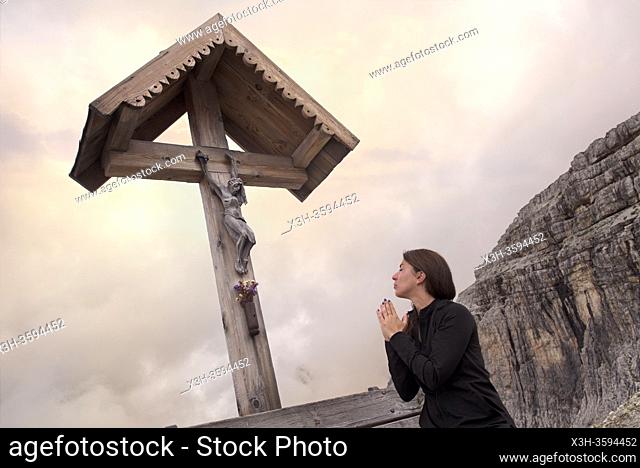 jeune femme priant assise sur un banc sous un crucifix sur le chemin reliant les refuges Locatelli (Dreizinnenhutte) et Pian di Cengia (Bullelejochhutte)