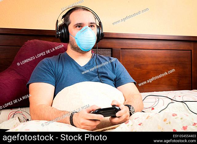 sick man with headphone and medical mask, playing videogames in the bed