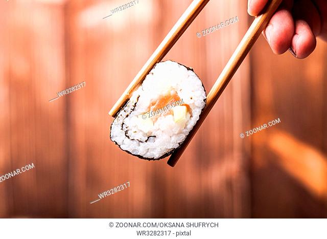 Sushi roll close up between pair of chopsticks