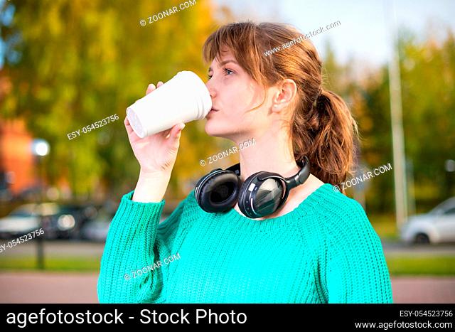 Happy young student woman drinking take away coffee and walking in an urban city park