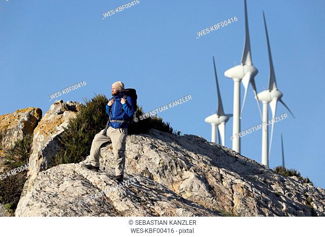 Spain, Andalusia, Tarifa, man on a hiking trip standing on rock with wind turbines in background