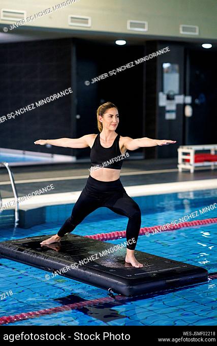 Woman with arms outstretched practicing yoga on raft in swimming pool
