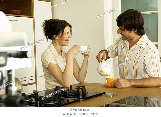 Young couple in kitchen, drinking tea, smiling
