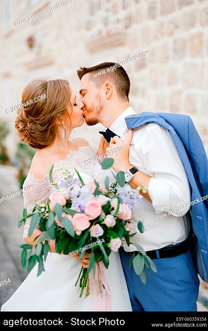 The bride and groom stand hugging and kissing near a beautiful brick house in the old town of Perast, close-up. High quality photo