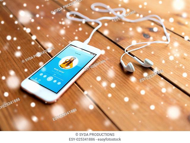technology, music, gadget and object concept - close up of white smartphone and earphones on wooden surface with media player on screen