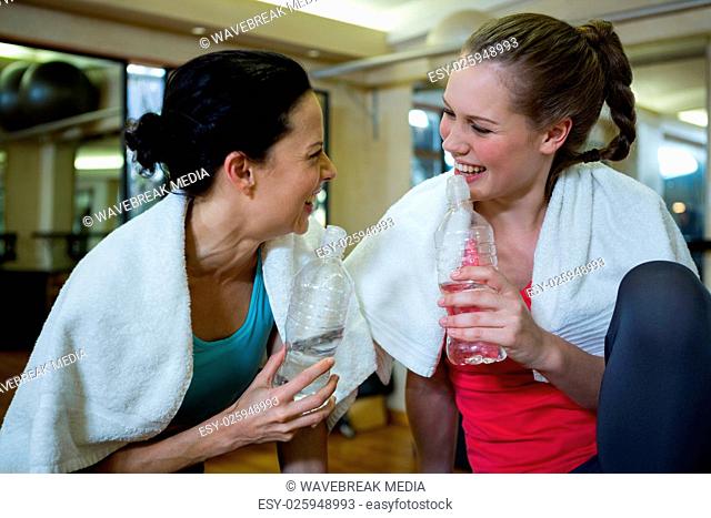 Happy women holding water bottle while relaxing after workout