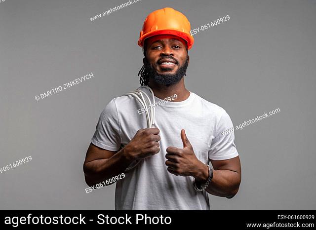 Waist-up portrait of a calm young man in an orange helmet making a thumbs-up gesture