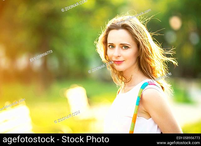 Portrait of lovely urban girl with backpack in the street. Happy smiling woman. Fashionable blonde girl walking in a city park