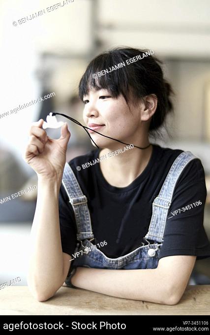 Korean woman sitting at table in cafe, looking at her pendant