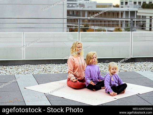 Daughters and mother meditating together on rooftop