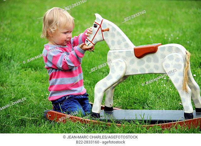 2 years old girl playing with a wooden horse