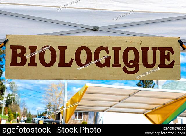 A close-up view of a French sign, saying biological, hanging over a market stall at an agricultural fair, blurry awnings are seen in background with copy space