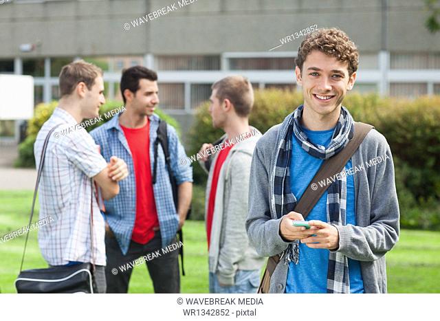 Cheerful male student sending a text in front of his classmates outside