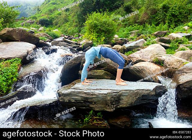 Yoga outdoors, young sporty fit woman doing Ashtanga Vinyasa Yoga asana Urdhva Dhanurasana, upward bow pose at tropical waterfall