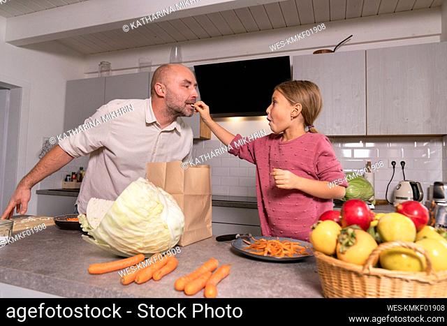 Daughter feeding father in kitchen at home
