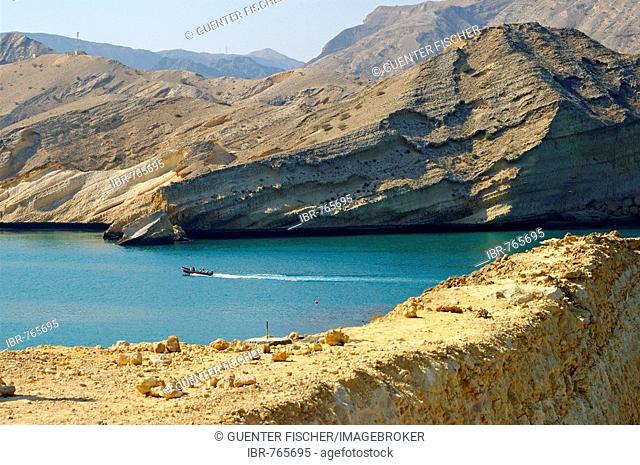 Motor boat on the Bay of Barr Al Jissah nestled between high arid rocky mountains, Muscat, Sultanate of Oman, Middle East