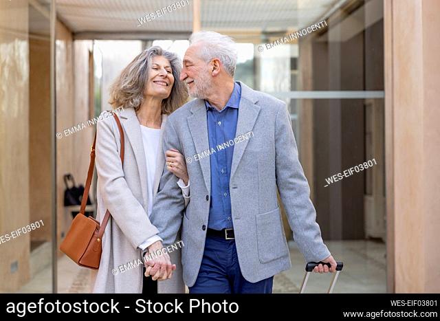 Smiling senior couple holding hands in lobby at boutique hotel
