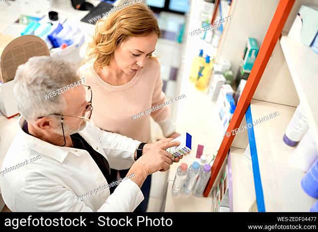 Pharmacist helping customer reading instruction on medicine box at pharmacy store