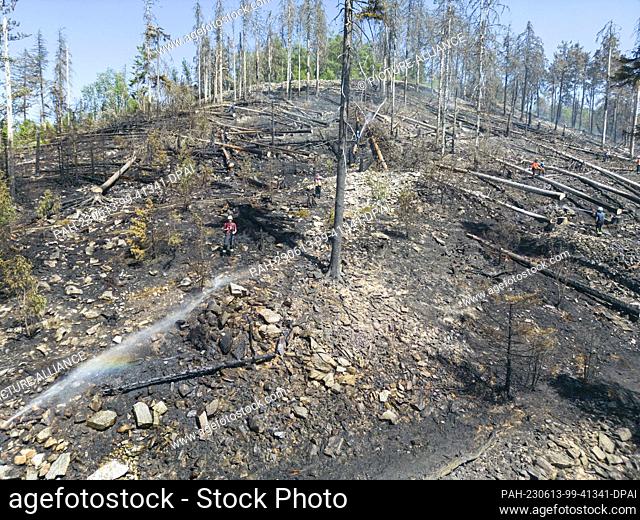 13 June 2023, Hesse, Oberursel: Firefighters extinguish nests of embers and flames flaring up again at a forest fire on the Altkönig in Taunus (aerial photo...