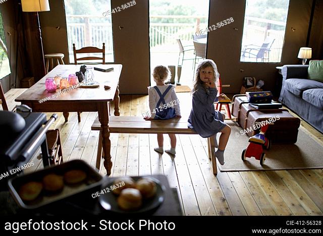 Cute sisters sitting on wood bench in dining room