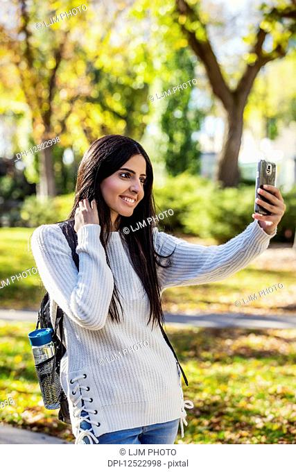 A young female university student of Lebanese ethnicity poses for a self-portrait using her smart phone; Edmonton, Alberta, Canada