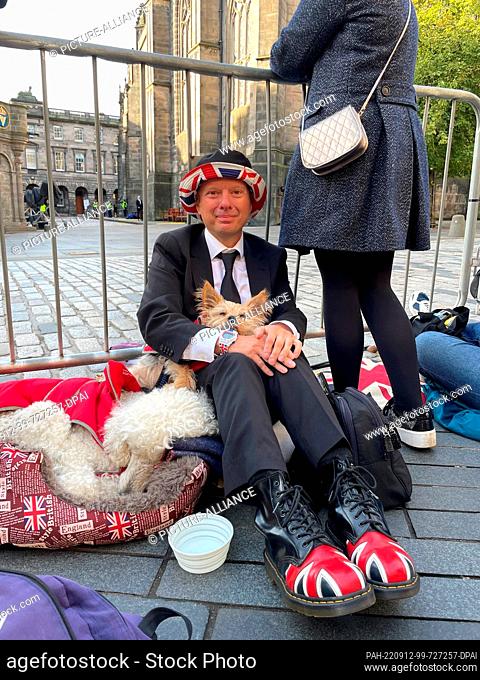 12 September 2022, Great Britain, Edinburgh: Denis Melvin from Wales waits with his two dogs in front of a barrier for the procession with the Queen's coffin
