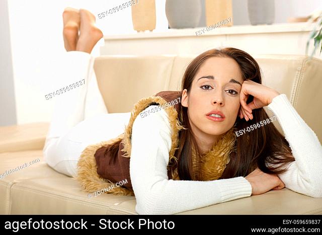Portrait of young woman lying on front in couch, looking at camera