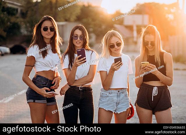 Four attractive women are standing on car parking and looking at their smartphones