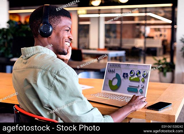 Smiling african american young businessman talking on phone while planning strategy on laptop