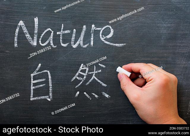 Nature - word written on a smudged blackboard with a Chinese translation, with a hand holding chalk