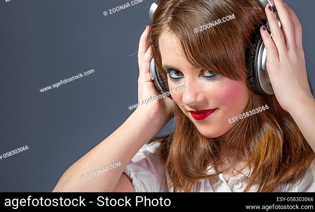 Entertainment redhead girl with helmet on her head listening to music on a flat gray background