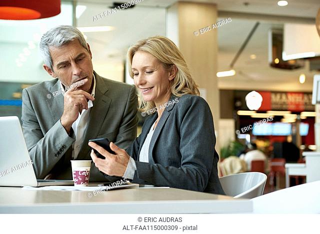 Businesspeople using smart phone in cafeteria