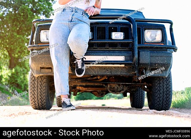 Woman leaning on vehicle hood during road trip