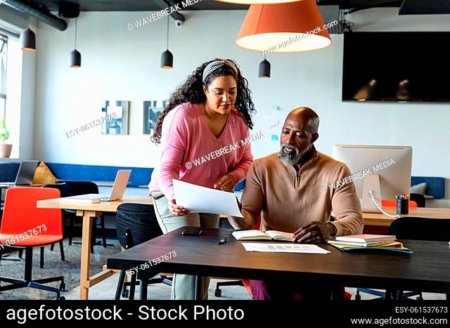 Multiracial businessman and businesswoman discussing over document in creative office